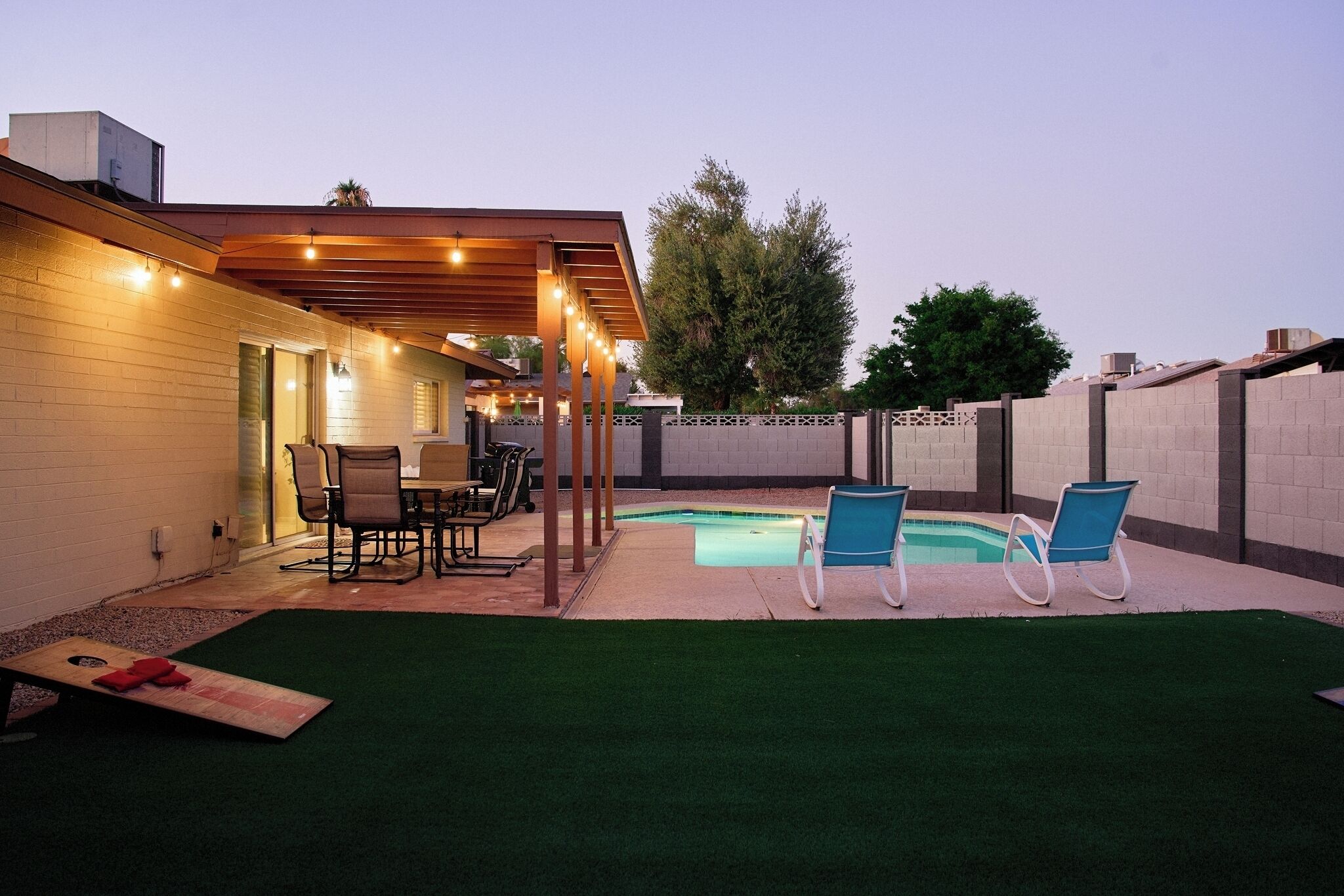 A backyard with a pool, artificial grass, and outdoor furniture.