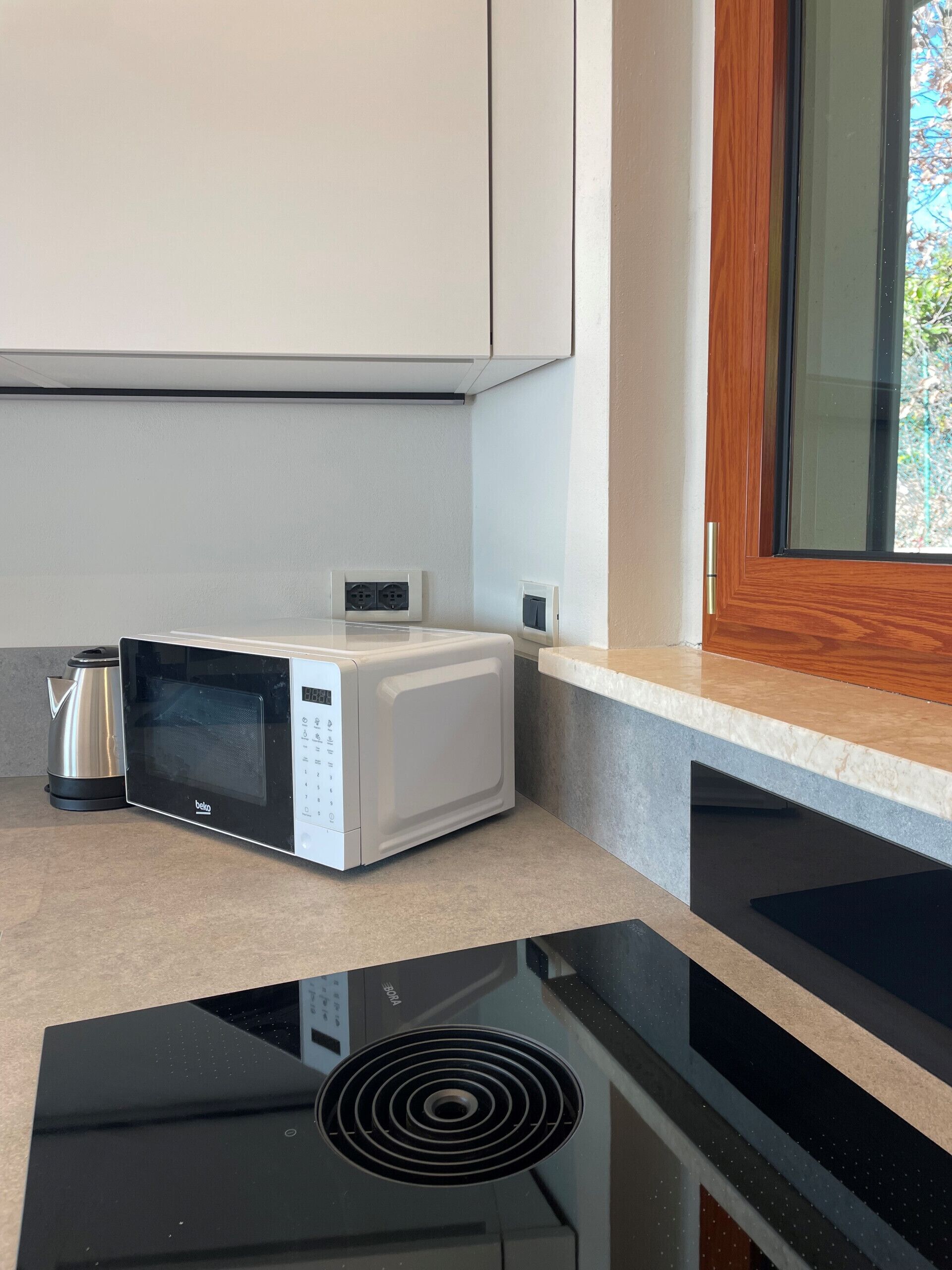 A kitchen with a microwave, kettle, and a black induction cooktop.