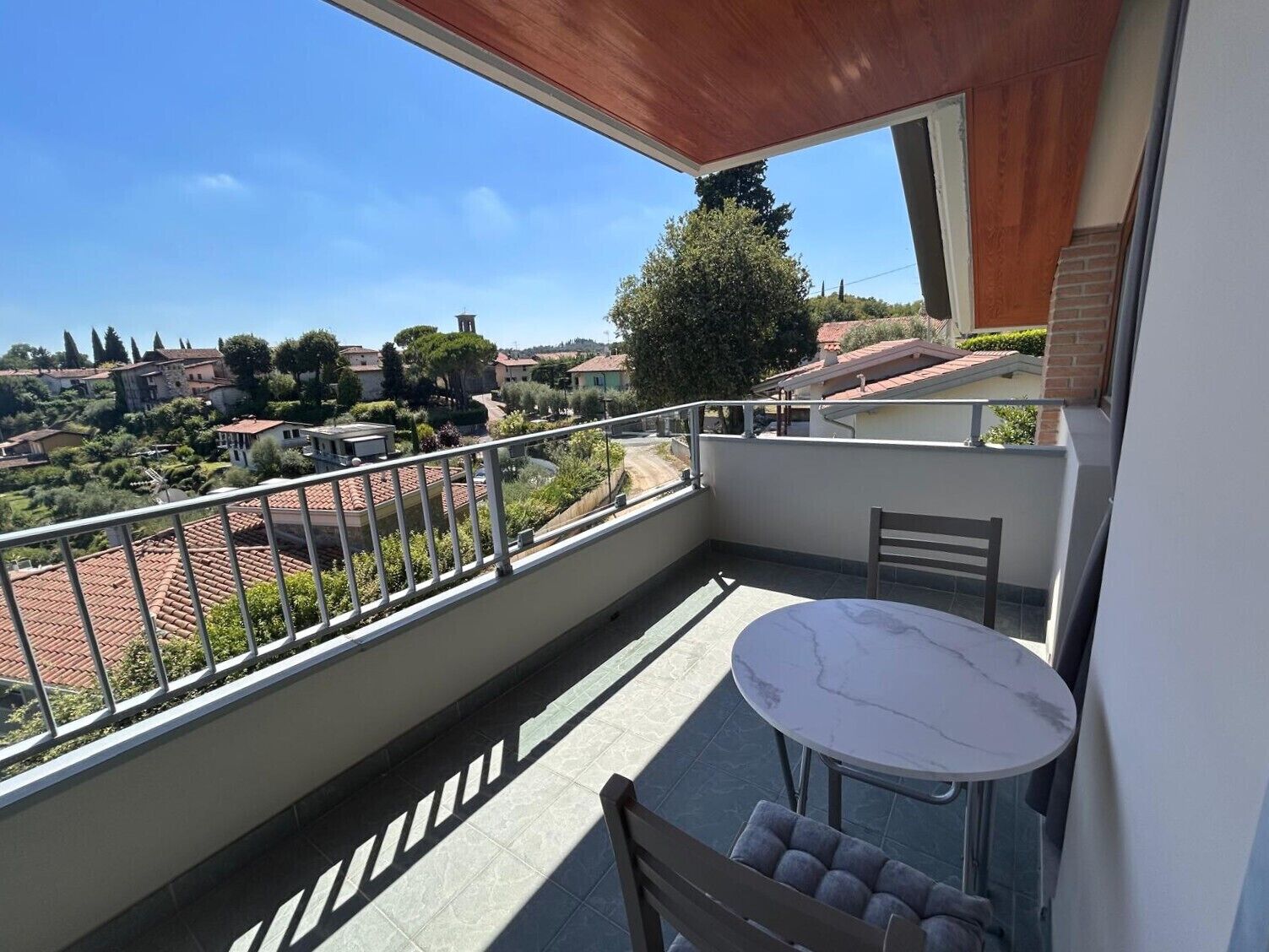 A balcony with a view of a town, a table, and a chair.