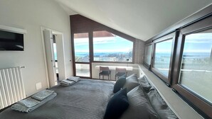 A bedroom with a large bed, a view of the city, and a balcony with a table and chairs. - Casa Pratello_Design and relax with a view of the lake (Padenghe sul Garda)