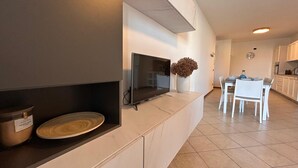 Ett modernt kök med en inbyggd TV, en matplats med vita stolar och en köksö med en vas med torkade blommor.