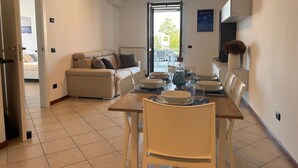 En matplats med ett bord för fyra personer, en soffa och utsikt genom en glasdörr ut till en uteplats.