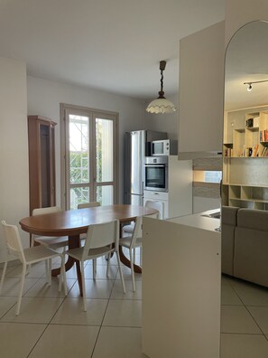 A modern kitchen with a dining area, featuring a large wooden table, white chairs, and built-in appliances.