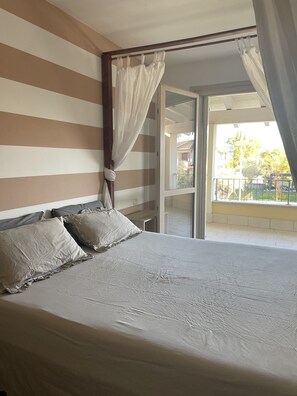 A bedroom with a bed, striped walls, and a balcony with a view.