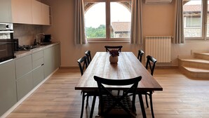 A modern kitchen with a wooden table and chairs, a built-in oven, and a view through a window. - Borgo Alba Lake View Loft_Design in the Historic Village (Polpenazze del Garda)