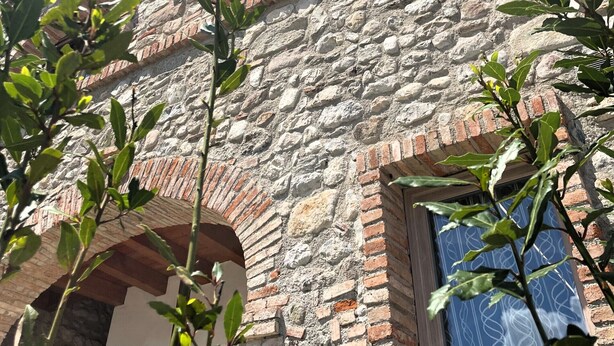 A stone building with arched windows and a door, surrounded by greenery. - Borgo Alba Lake View Loft_Design in the Historic Village (Polpenazze del Garda)