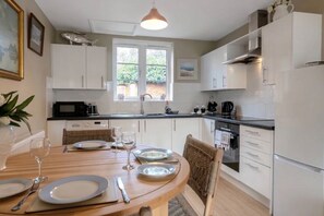 A modern kitchen with white cabinets, a dining table set for four, and a window providing natural light.
