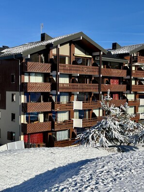 A multi-story hotel with balconies, a snow-covered ground, and a clear blue sky. - Charming apartment for 6-7 people, mountain view, ski slope nearby (Morillon)