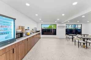 A modern kitchen with a refrigerator, microwave, and coffee maker. There is a large window with a view of buildings and trees.