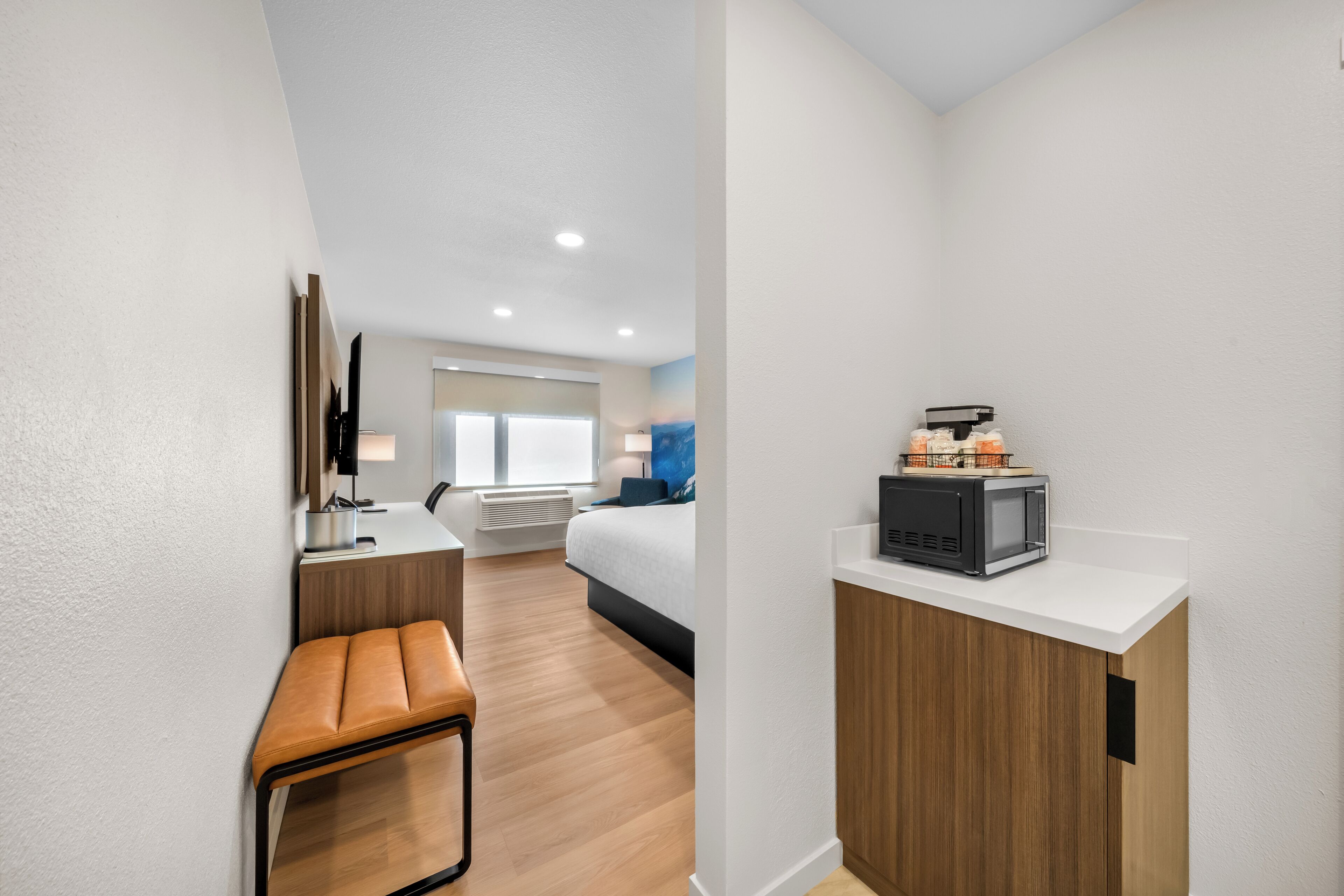 Ein kleines Hotelzimmer mit Küchenzeile, einem Bett, einem Schreibtisch und einer Sitzecke.