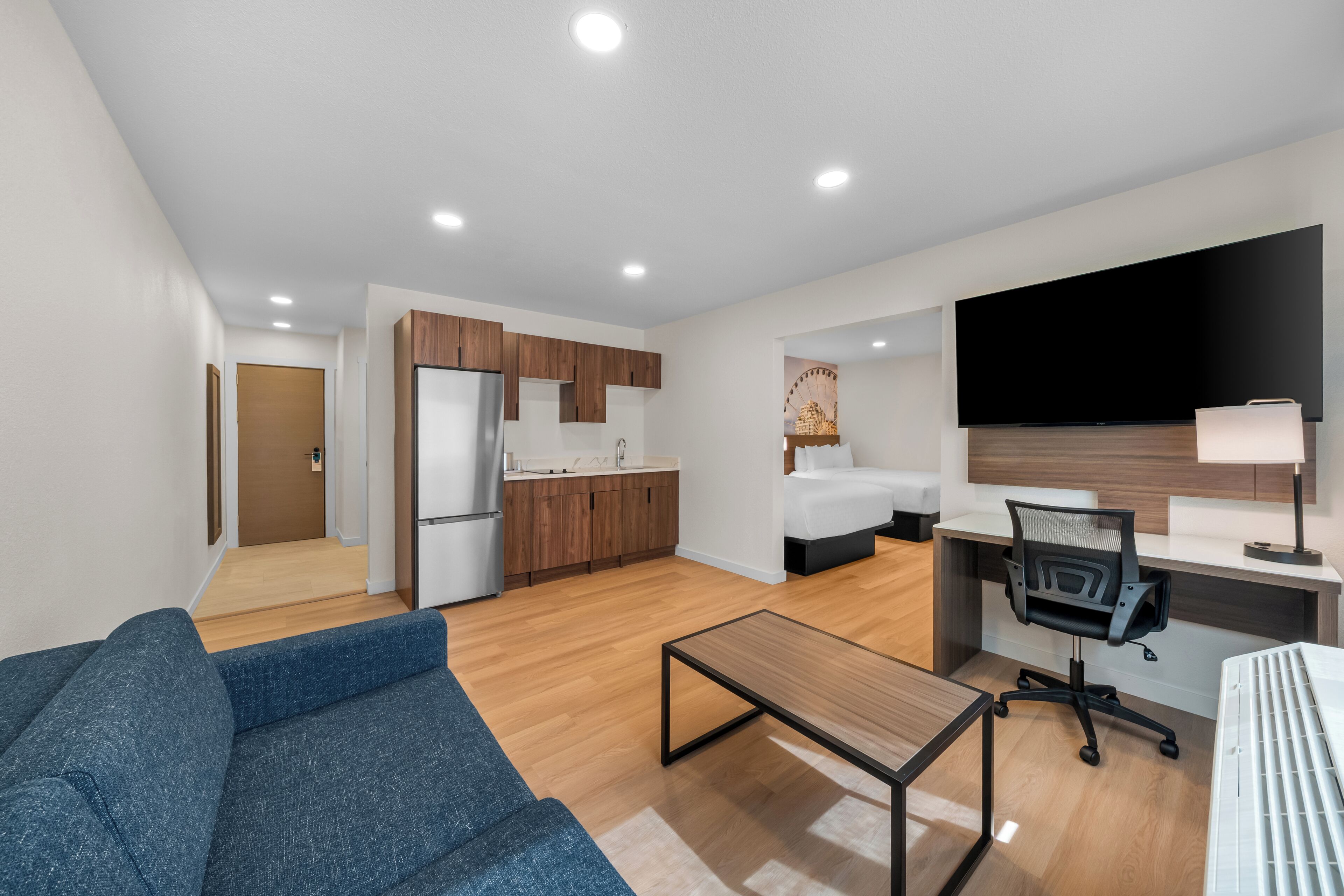Una habitación de hotel moderna con sofá, escritorio, televisión de pantalla plana, cama y kitchenette.