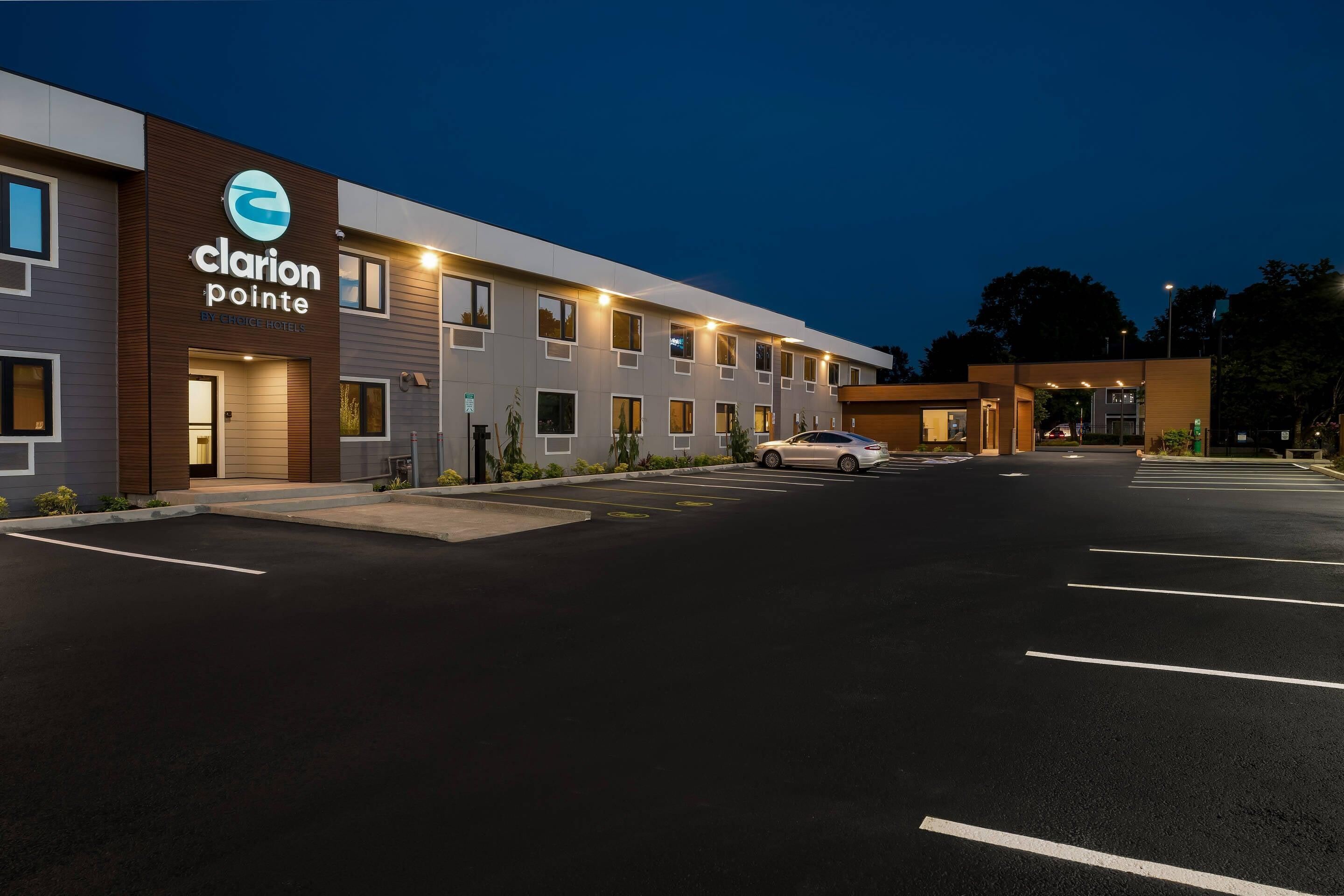 Un hotel Clarion Pointe con diseño moderno, un estacionamiento y un coche estacionado al frente.