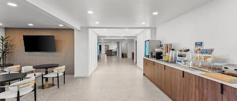 A modern hotel lobby with a reception desk, seating area, and a TV mounted on the wall.