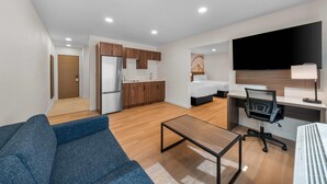 Une chambre d’hôtel moderne équipée d’un canapé, d  ’un bureau avec un ordinateur, d’un lit, d’une télévision et d’une kitchenette.