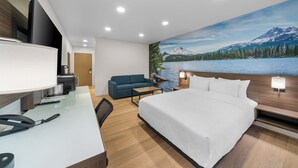 Habitación de hotel moderna con cama, escritorio y zona de estar, que ofrece vistas a una montaña y un lago.