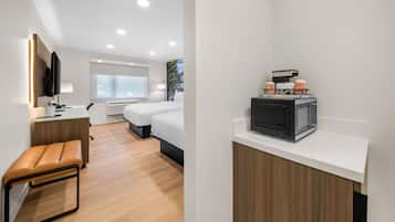 Une chambre d’hôtel moderne équipée d’une télévision à écran plat, d’un bureau avec une lampe, d’un banc, d’un lit et d’une machine à café.