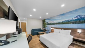Une chambre d’hôtel avec un lit, un bureau, une chaise et un tableau représentant un paysage de montagne.