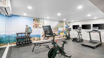 A gym with exercise equipment, a wall mural, and a treadmill.