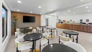 Un espace intérieur moderne avec des tables et des chaises rondes, un téléviseur à écran plat, un mur recouvert de panneaux en bois et un comptoir d’accueil.