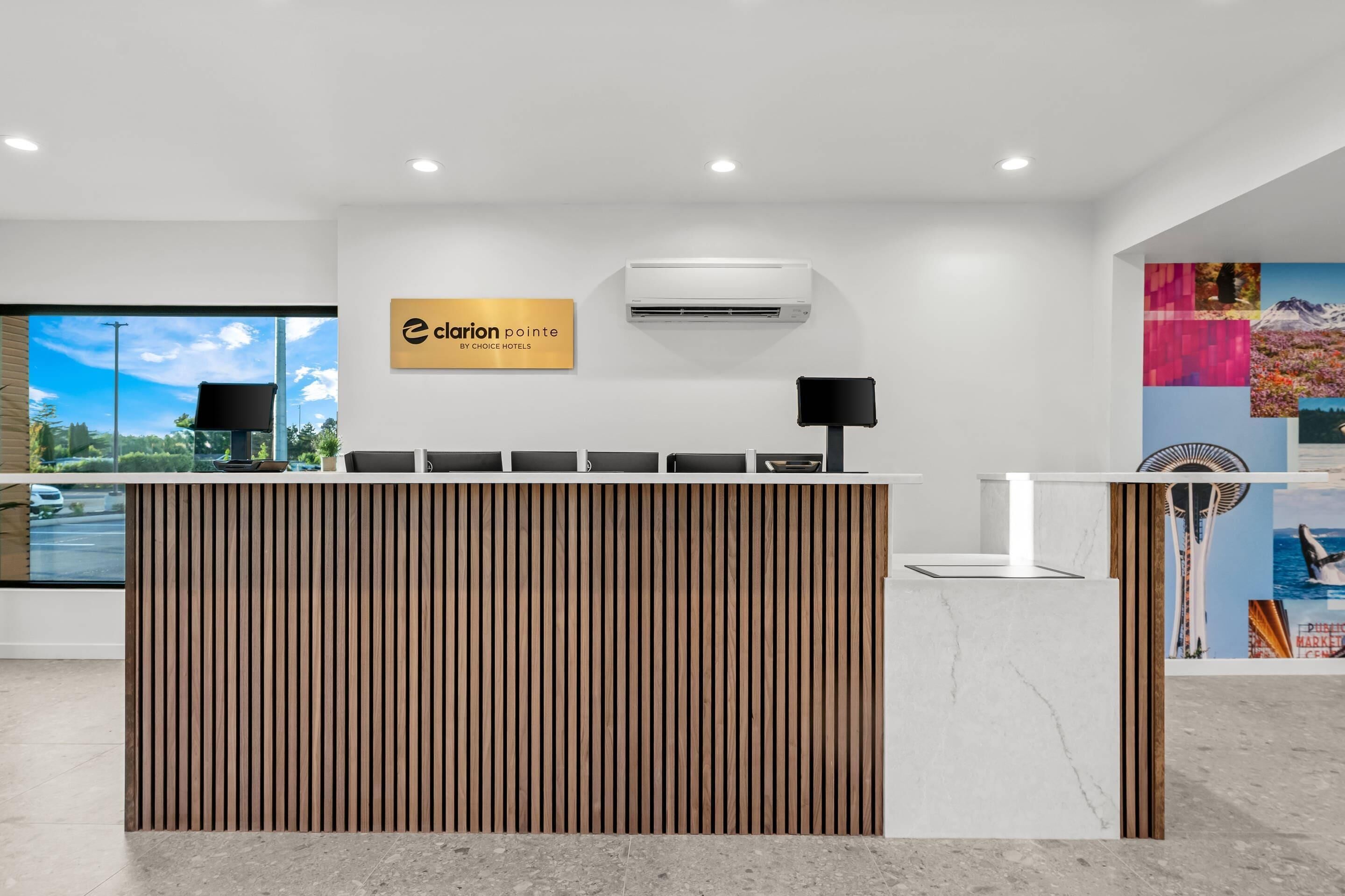 A reception desk with a wooden slat design, a sign for Clarion Pointe by Choice Hotels, and an air conditioning unit above.