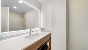 A modern bathroom with a large mirror, a white sink, and a wooden vanity.