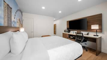 Une chambre d’hôtel avec un grand lit, un bureau doté d’un téléviseur à écran plat, un four à micro-ondes et une chaise.