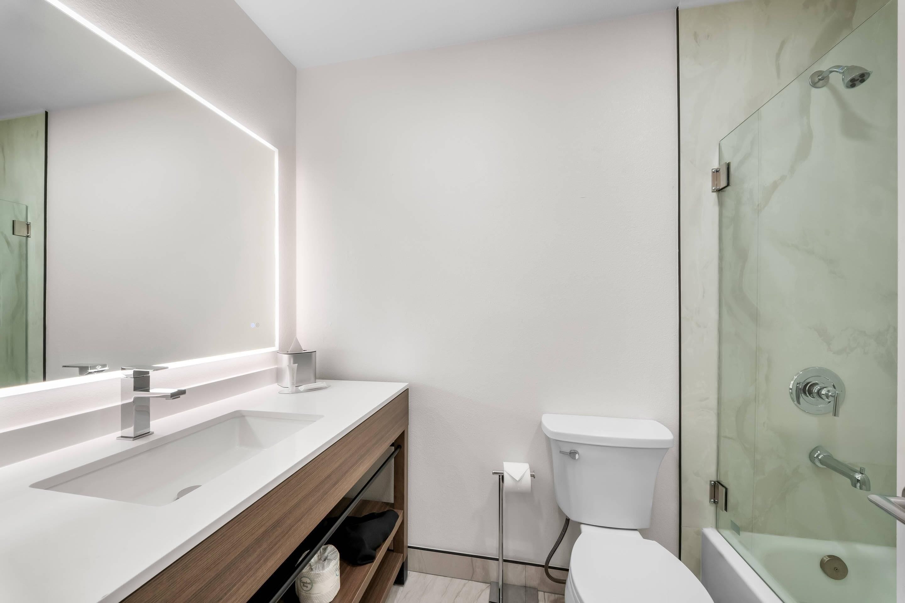 A modern bathroom with a large mirror, a white sink, a toilet, and a glass-enclosed shower.