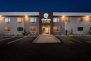 A hotel with a modern facade, a prominent logo, and a parking lot with marked spaces. - Clarion Pointe Kent - Seattle South (Kent)