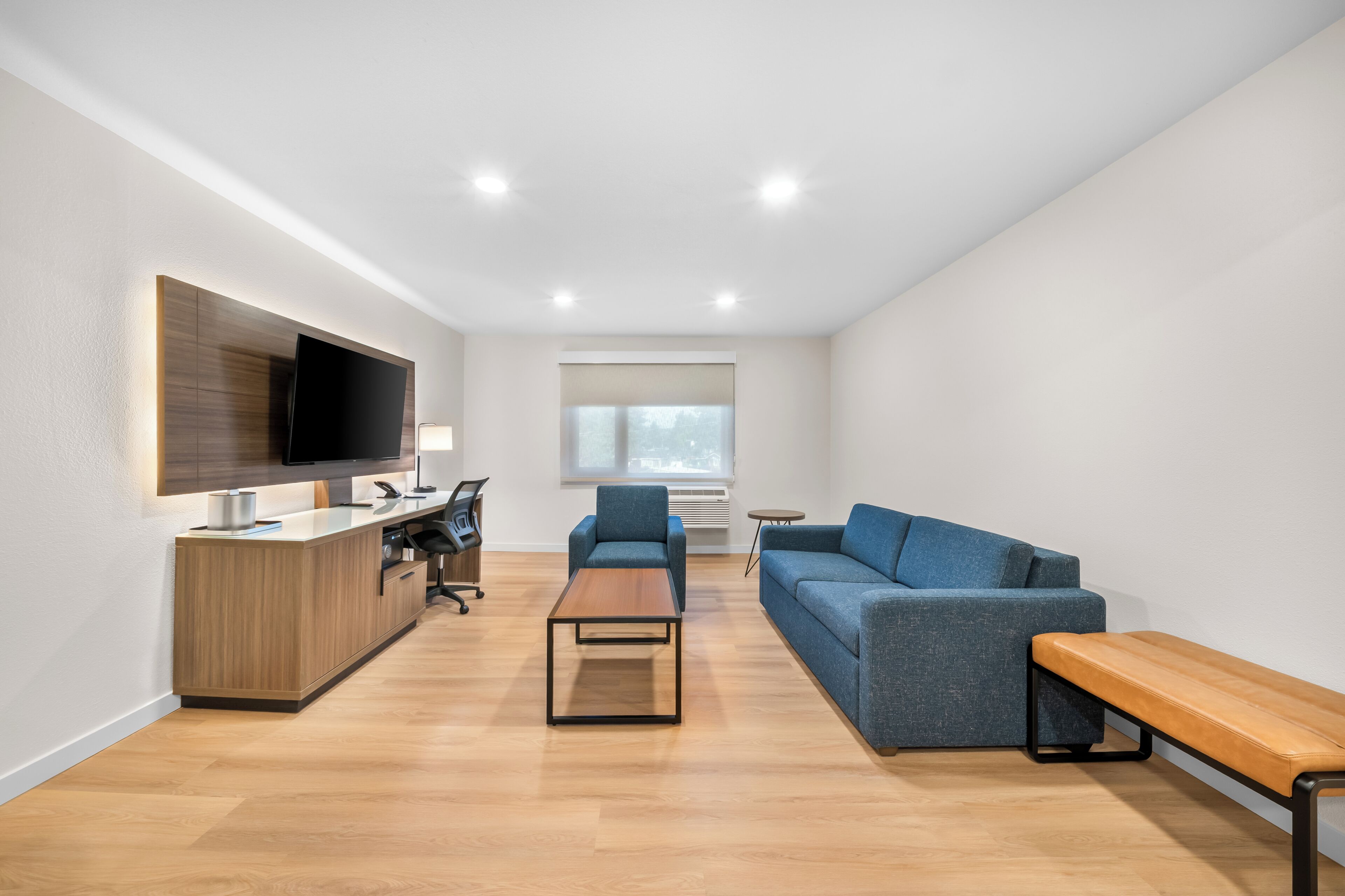 Una sala moderna con sofá, mesa de centro, banqueta, televisor y escritorio con computadora.