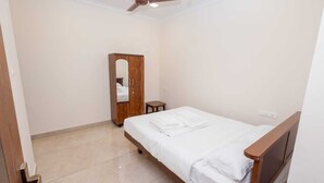 A bedroom with a bed, a wooden wardrobe, a small table, and a ceiling fan.