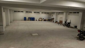 A spacious, unfinished interior with concrete floors and white walls, featuring several blue barrels, a ladder, and a motorcycle.