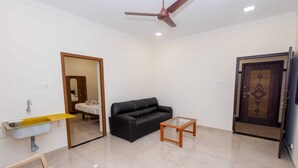 A living room with a black sofa, a glass coffee table, a yellow shelf, a white sink, and a ceiling fan.