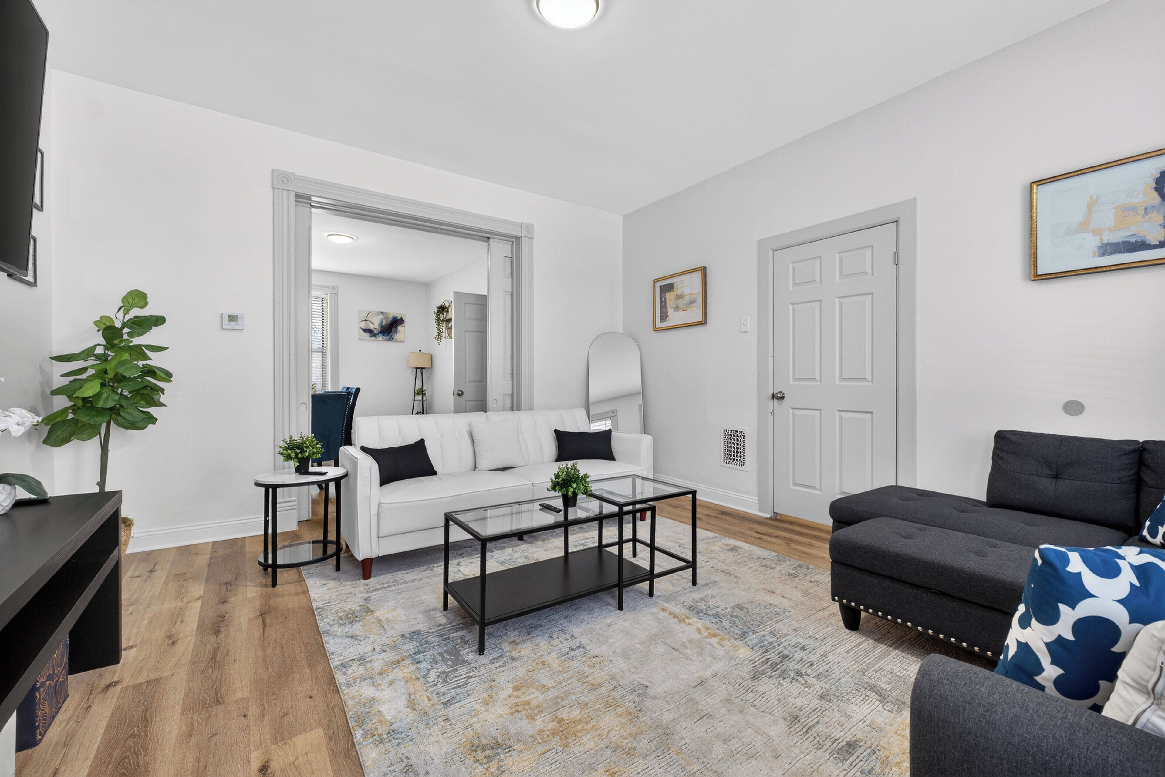 Ein modernes Wohnzimmer mit einem weißen Sofa, einem dunkelgrauen Sofa, einem Glastisch und einem gemusterten Teppich.