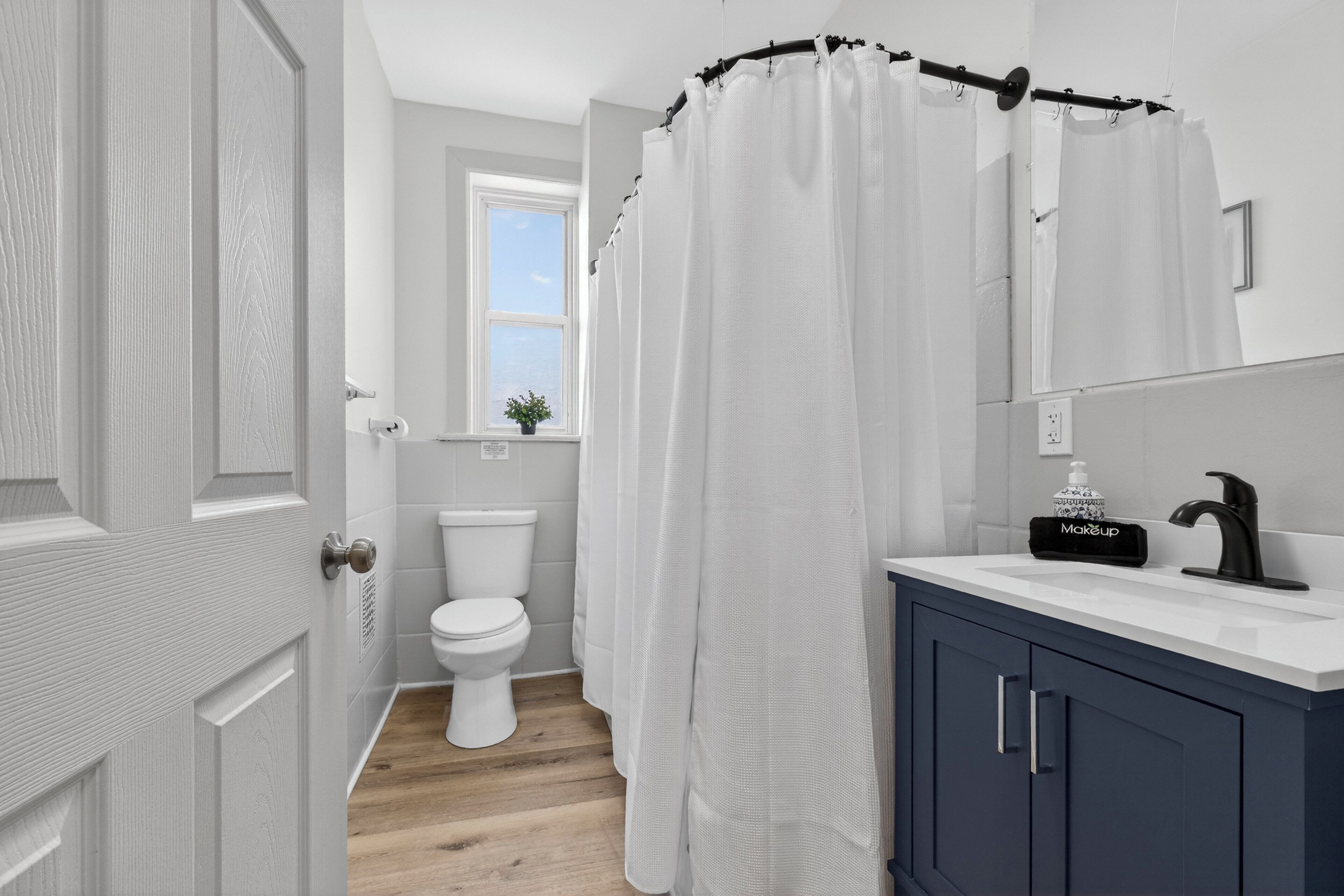 A bathroom with a white toilet, a shower curtain, a sink with a makeup dispenser, and a cabinet.