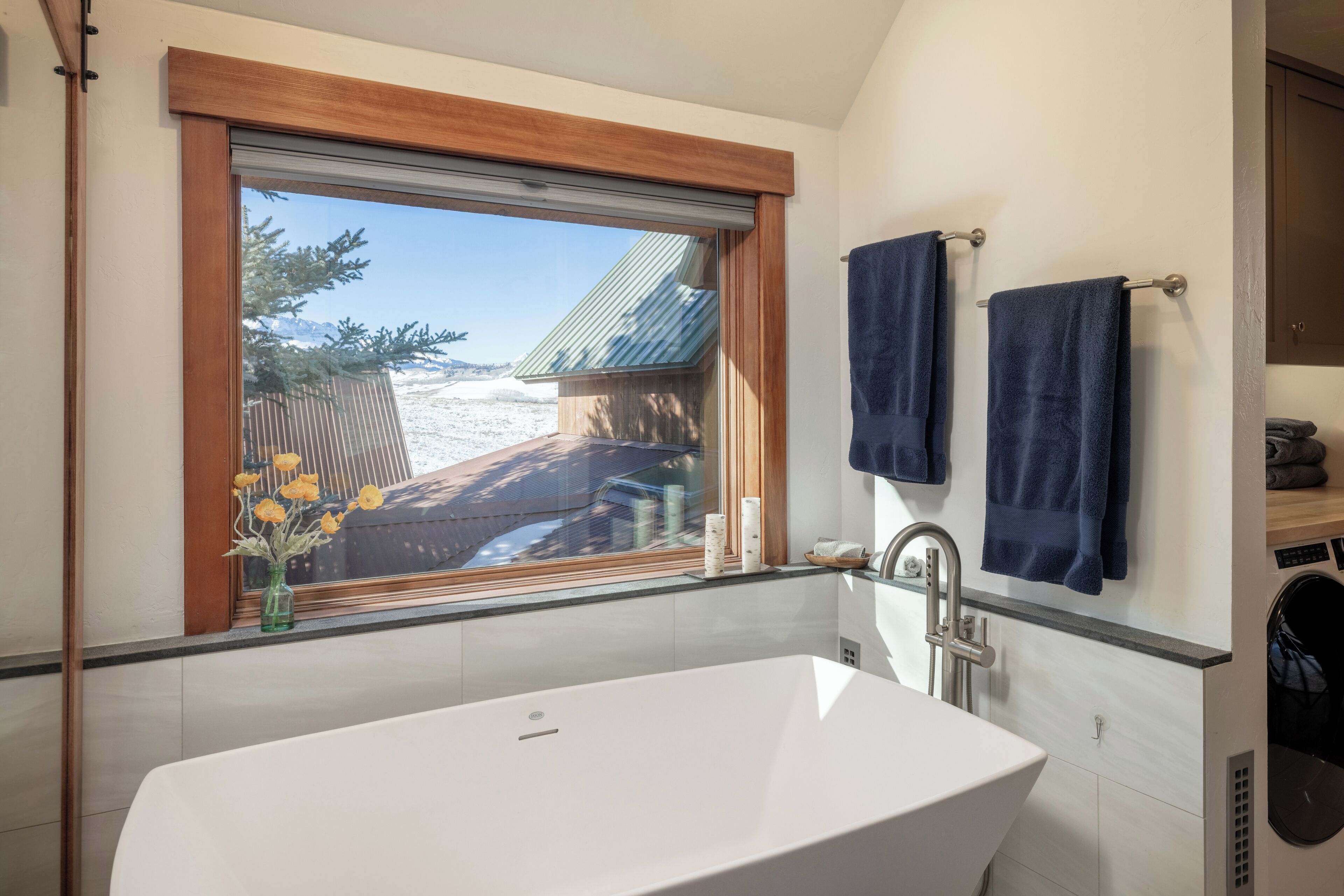 A modern bathroom with a freestanding bathtub, a window with a view of a snowy landscape, and two towels hanging on a rack.