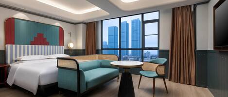 Ein Hotelzimmer mit Bett, einer Sitzecke, einem kleinen Tisch und Blick auf hohe Gebäude.