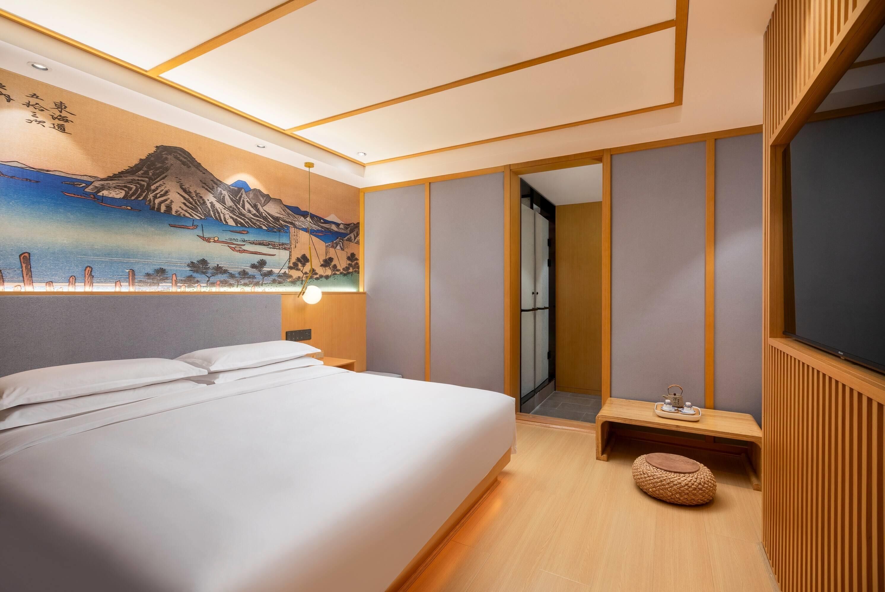 Une chambre d’hôtel avec un lit, une table de chevet, une lampe fixée au mur, un tableau et un plancher en bois.