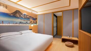 A hotel room with a bed, a nightstand, a wall-mounted lamp, a painting, and a wooden floor.