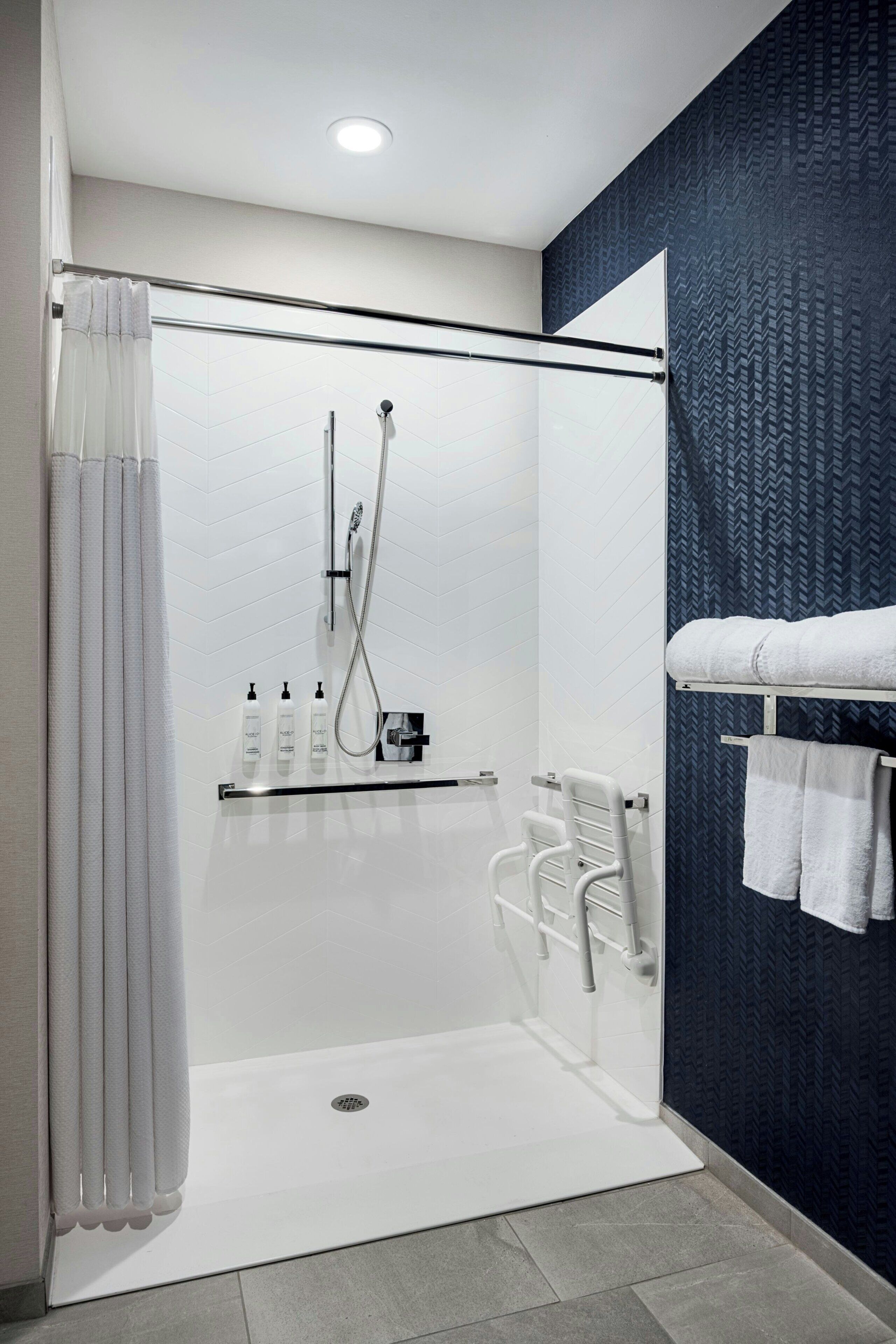 A modern shower area with a glass door, a towel rack, and a shelf with toiletries.
