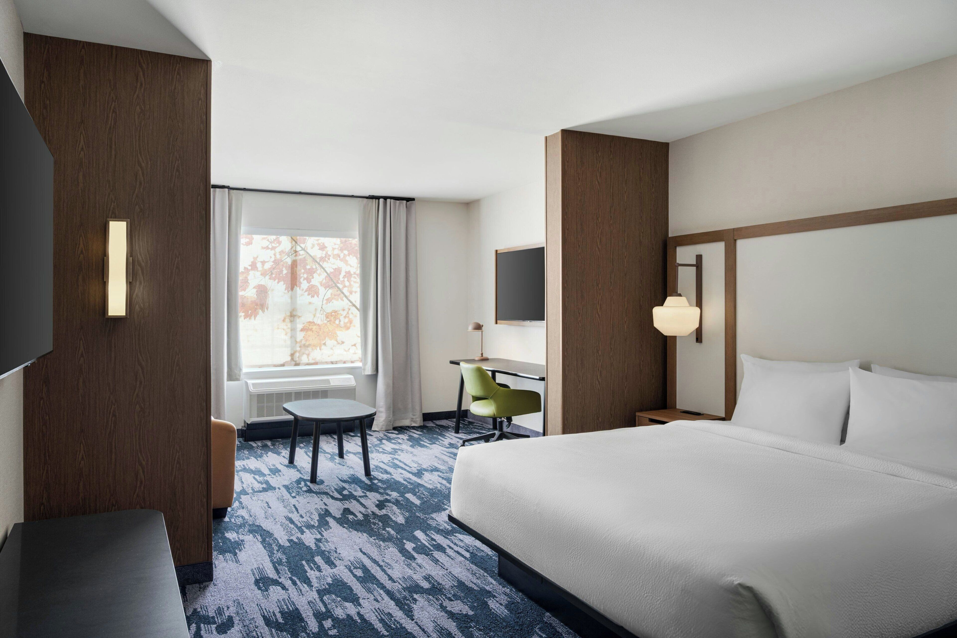 Une chambre d’hôtel avec un grand lit, un bureau, une chaise, une télévision et une fenêtre avec des rideaux.