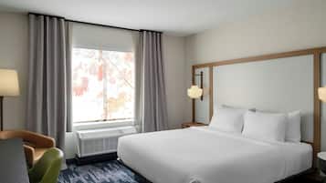 Habitación de hotel con cama, una silla, escritorio, lámpara y ventana con cortinas.