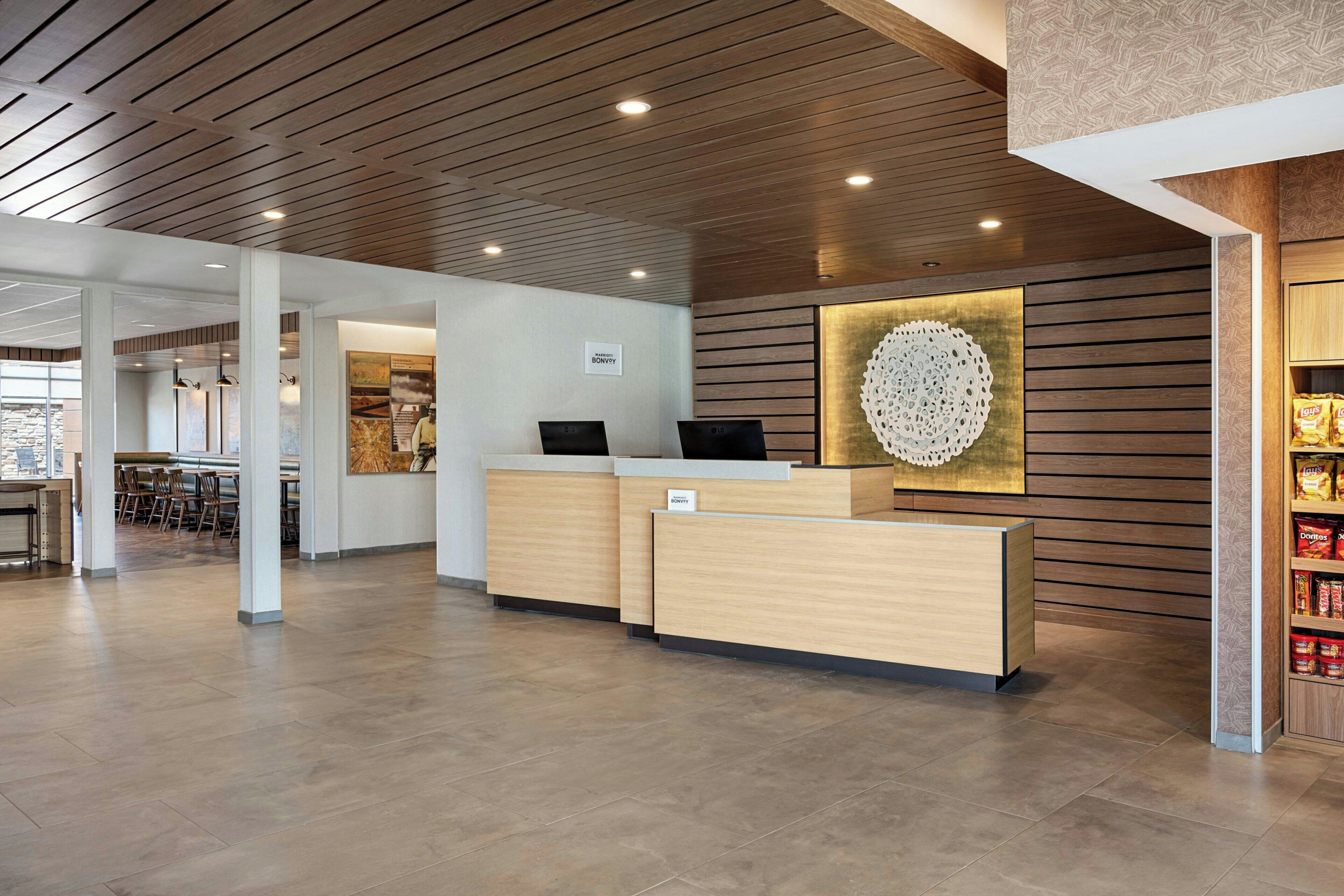 A hotel reception area with a wooden reception desk, a wall-mounted decorative piece, and a seating area with tables and chairs.