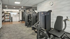 A gym with exercise equipment, a clock on the wall, and a weight rack.