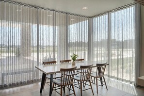 A dining area with a table and chairs, large windows with sheer curtains, and a view of an outdoor area. - Fairfield by Marriott Inn & Suites Mattoon (Mattoon)