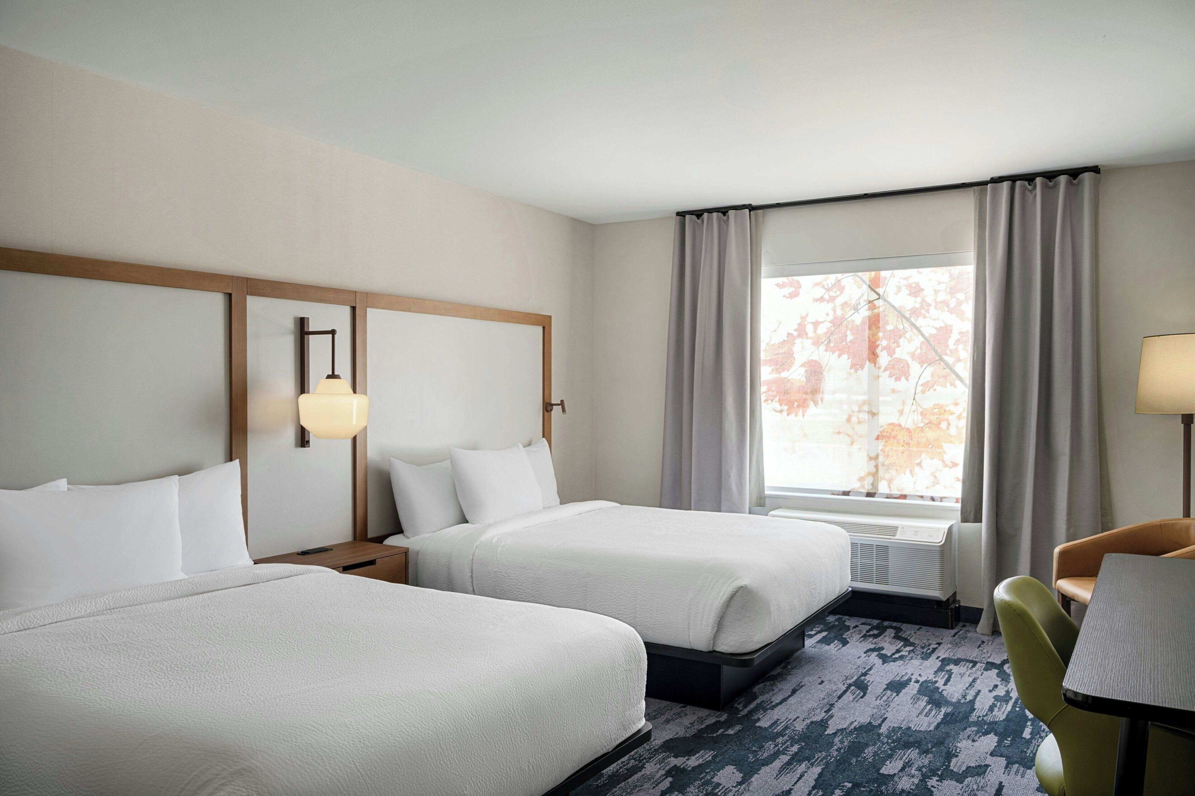 A hotel room with two beds, a desk, a chair, and a window with curtains.