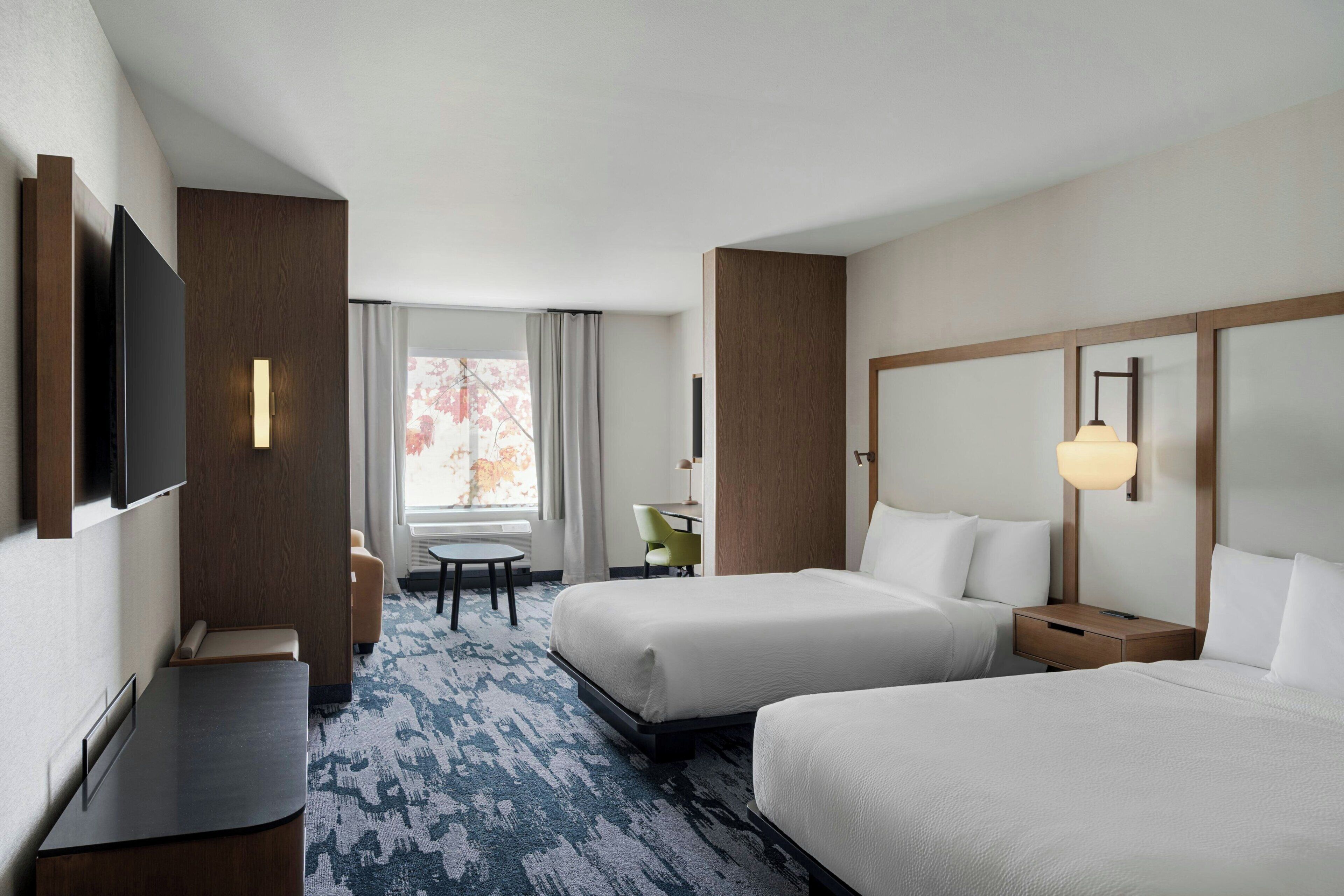 Habitación de hotel con dos camas, un escritorio, una silla, un televisor y una ventana con cortinas.