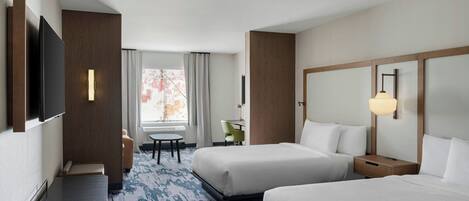 Habitación de hotel con dos camas, un escritorio, una silla, un televisor y una ventana con cortinas.