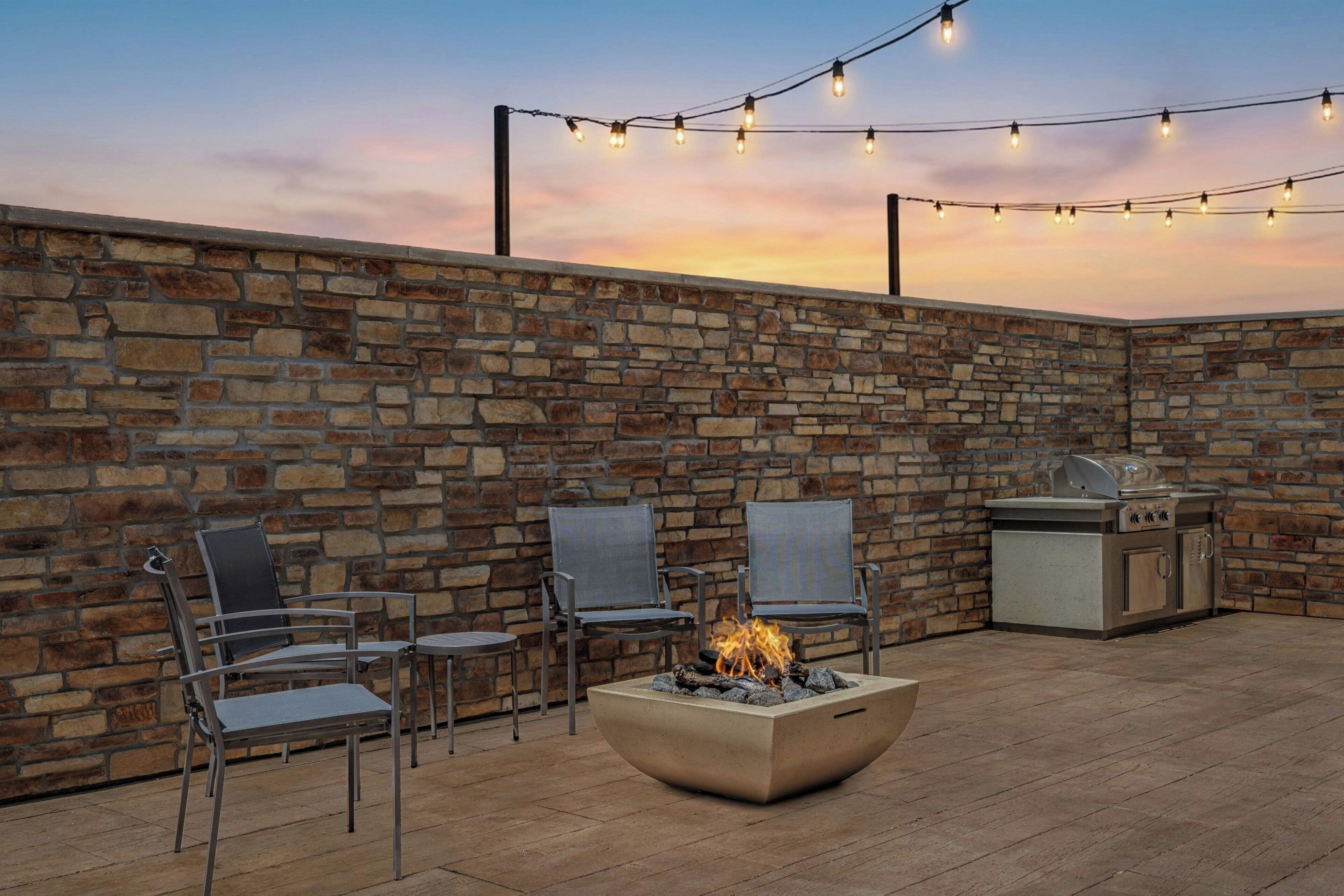 An outdoor patio with stone walls, a fire pit, metal chairs, and a grill.