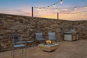 An outdoor patio with stone walls, a fire pit, metal chairs, and a grill. - Fairfield by Marriott Inn & Suites Mattoon (Mattoon)