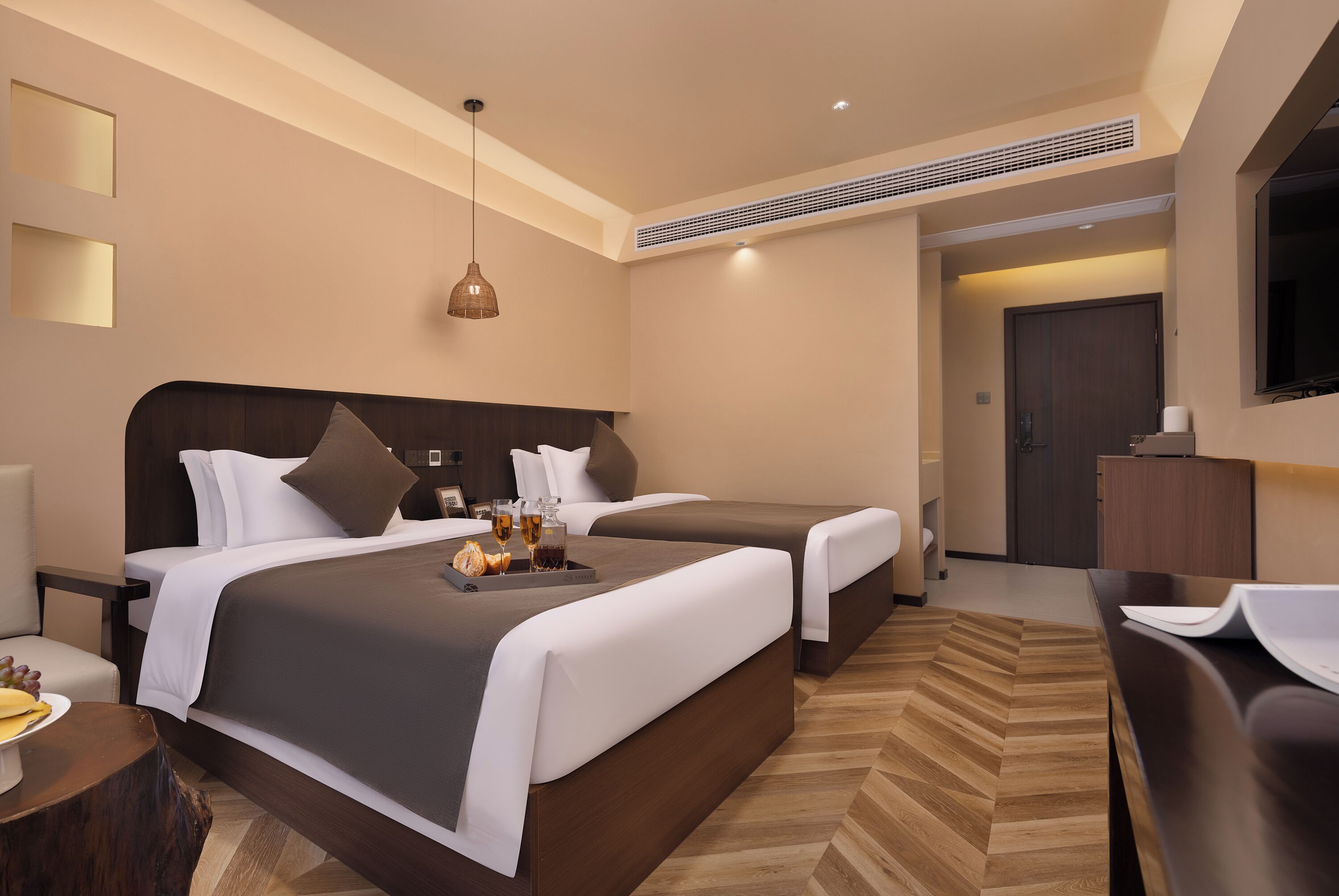 A hotel room with two beds, a wooden herringbone floor, a desk, and a television.